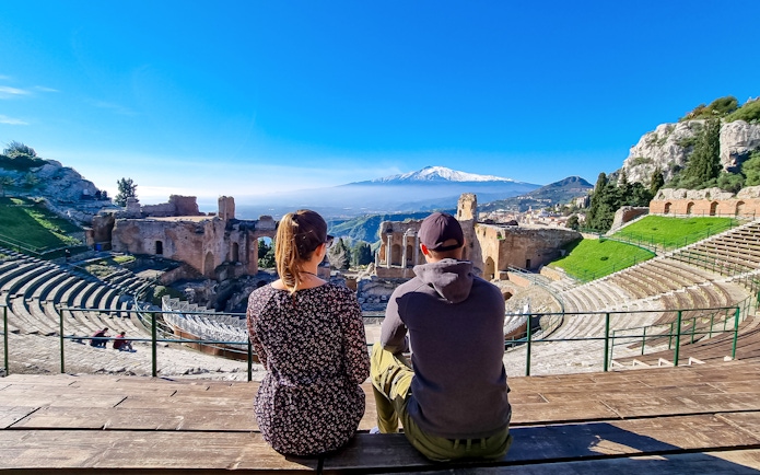 Couple sitting with view of Mount Etna from ancient Greek theater in Taormina, Sicily.