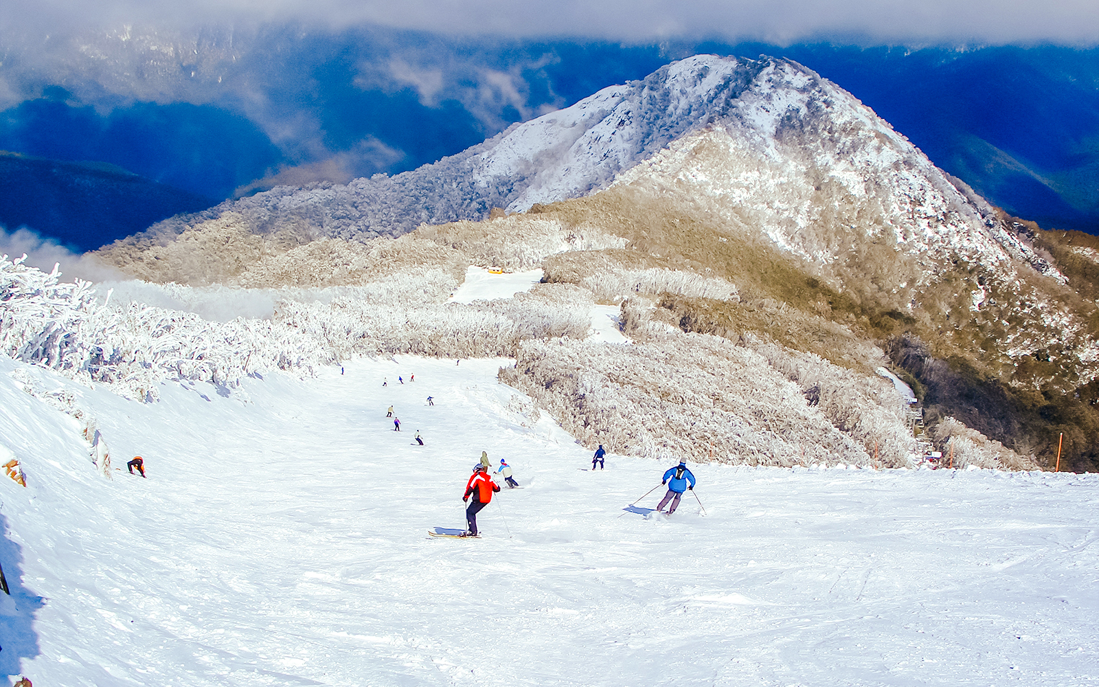 Skiers descending a snowy slope on Mt Buller, Australia, with a mountain backdrop.