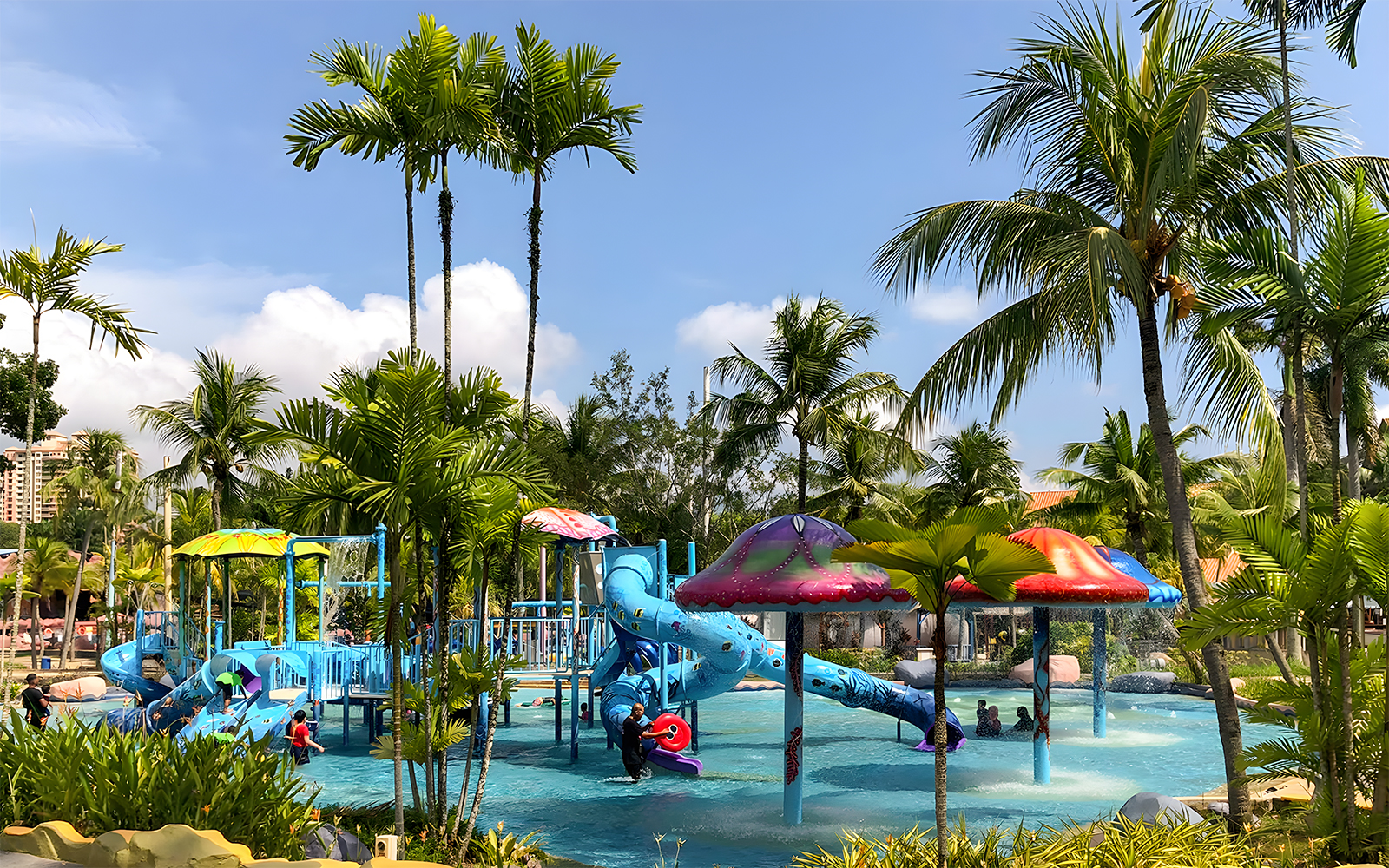 Family enjoying water slides at A'Famosa Melaka Waterpark, Malaysia, surrounded by palm trees.