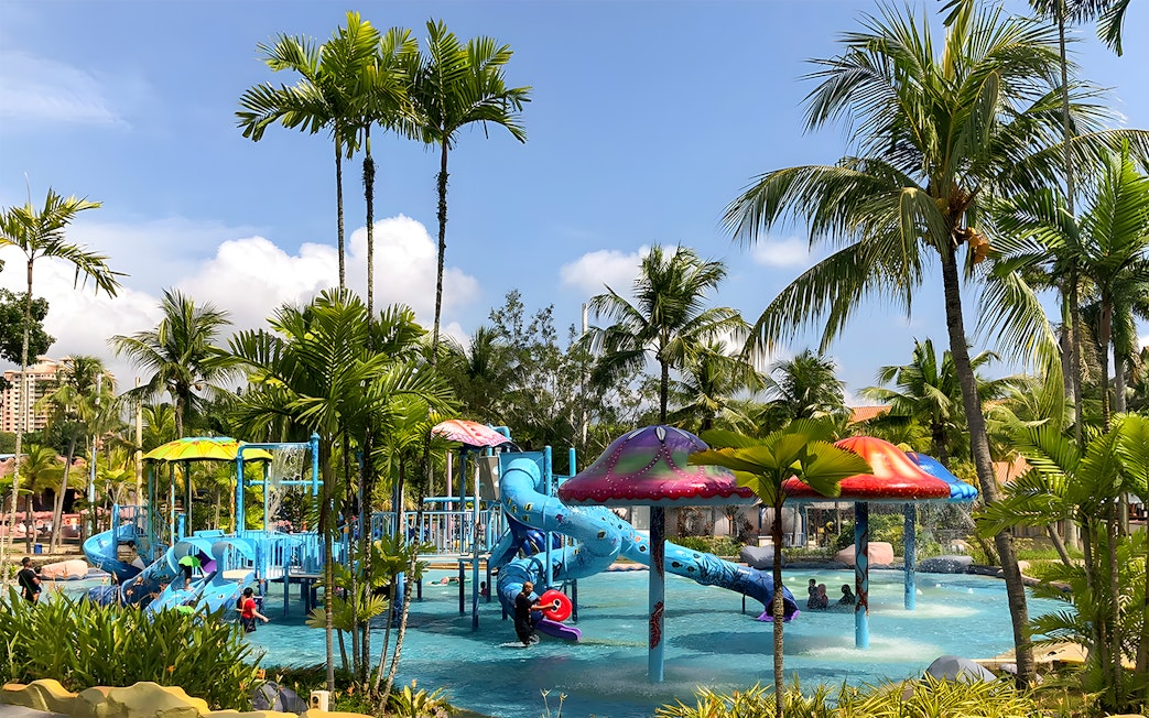Family enjoying water slides at A'Famosa Melaka Waterpark, Malaysia, surrounded by palm trees.