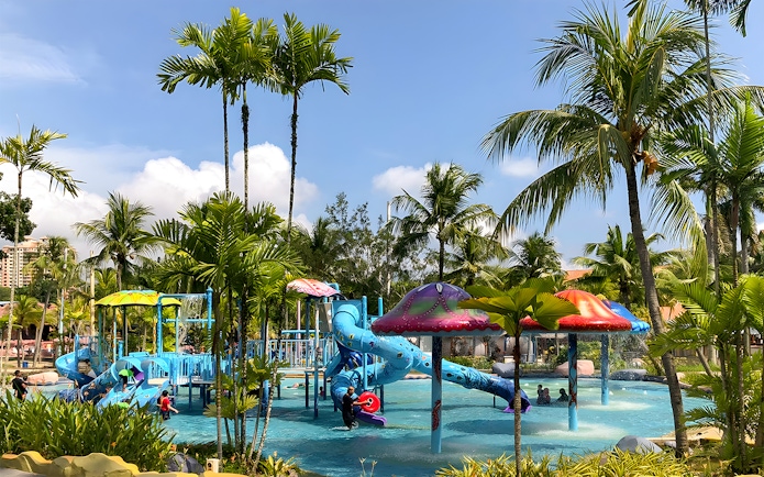Family enjoying water slides at A'Famosa Melaka Waterpark, Malaysia, surrounded by palm trees.