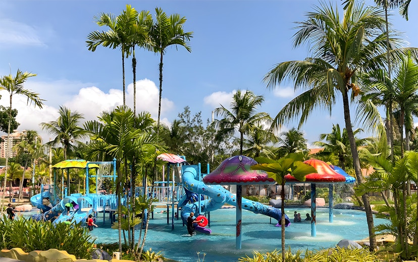 Family enjoying water slides at A'Famosa Melaka Waterpark, Malaysia, surrounded by palm trees.