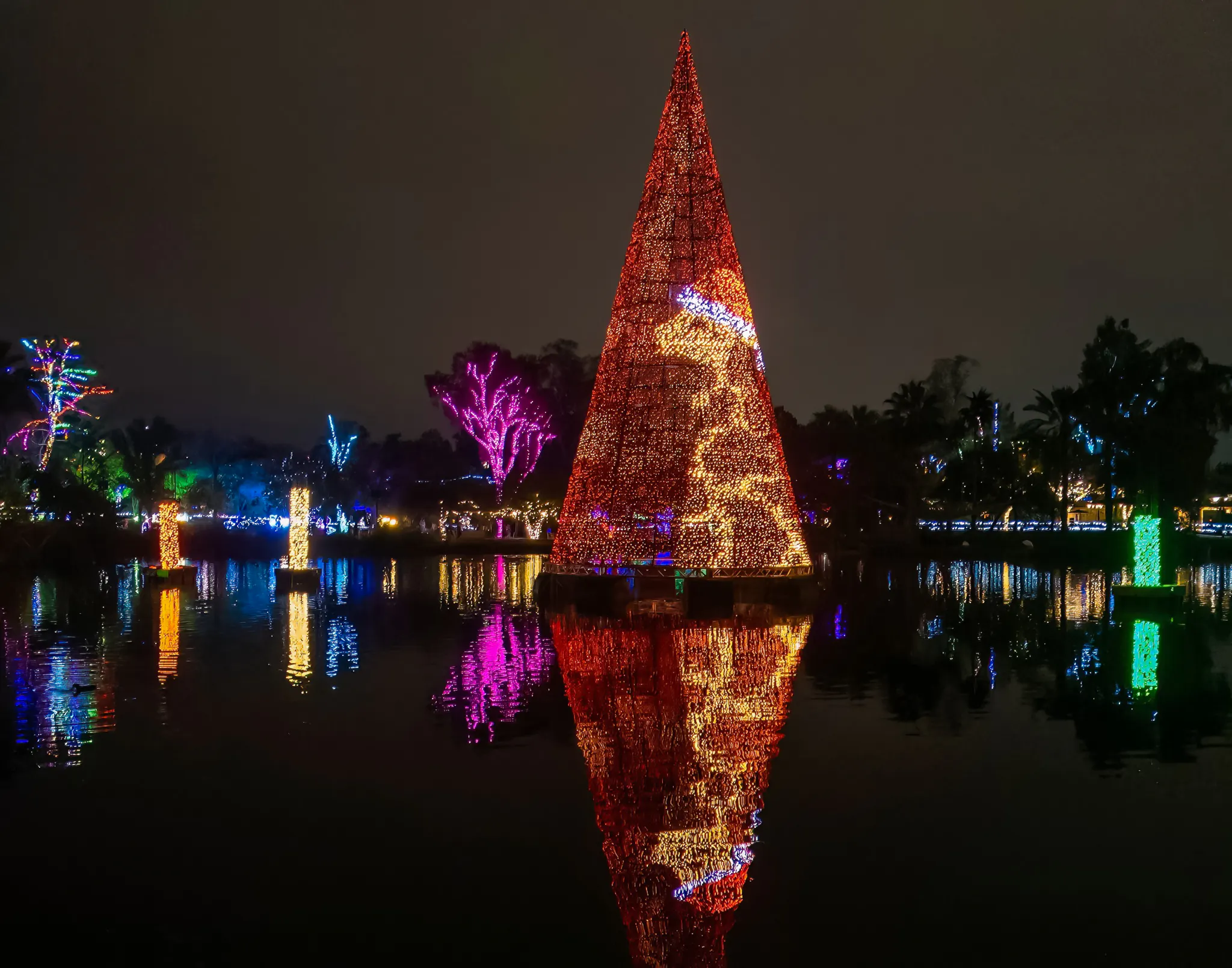 Holiday lights display at Phoenix Zoo with colorful reflections on water.