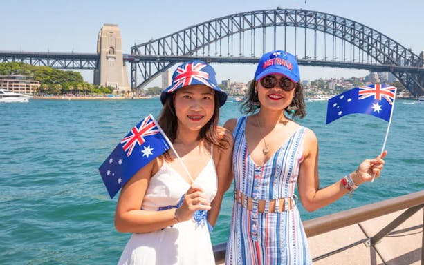 Two people holding Australian flags with Sydney Harbour Bridge in the background.