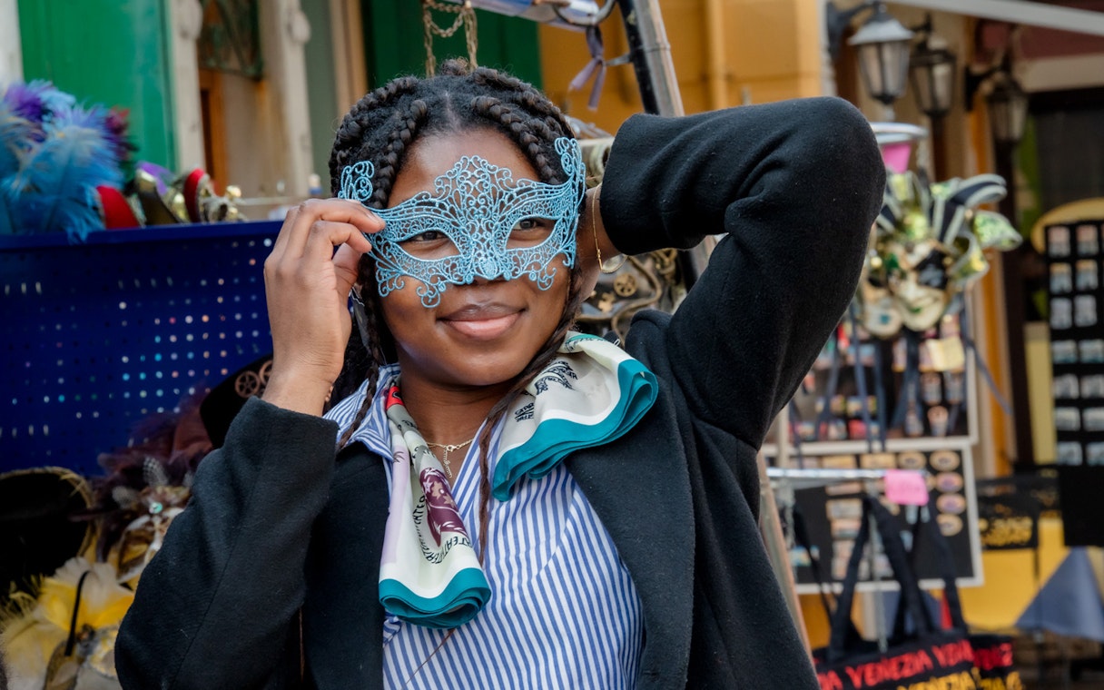Person holding a blue lace mask at a Torcello market stall.