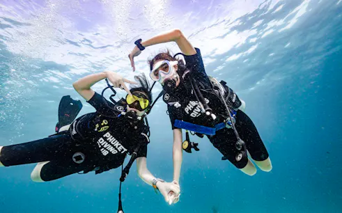 Scuba divers underwater at Racha Island, Phuket, holding hands during a beginner dive trip.