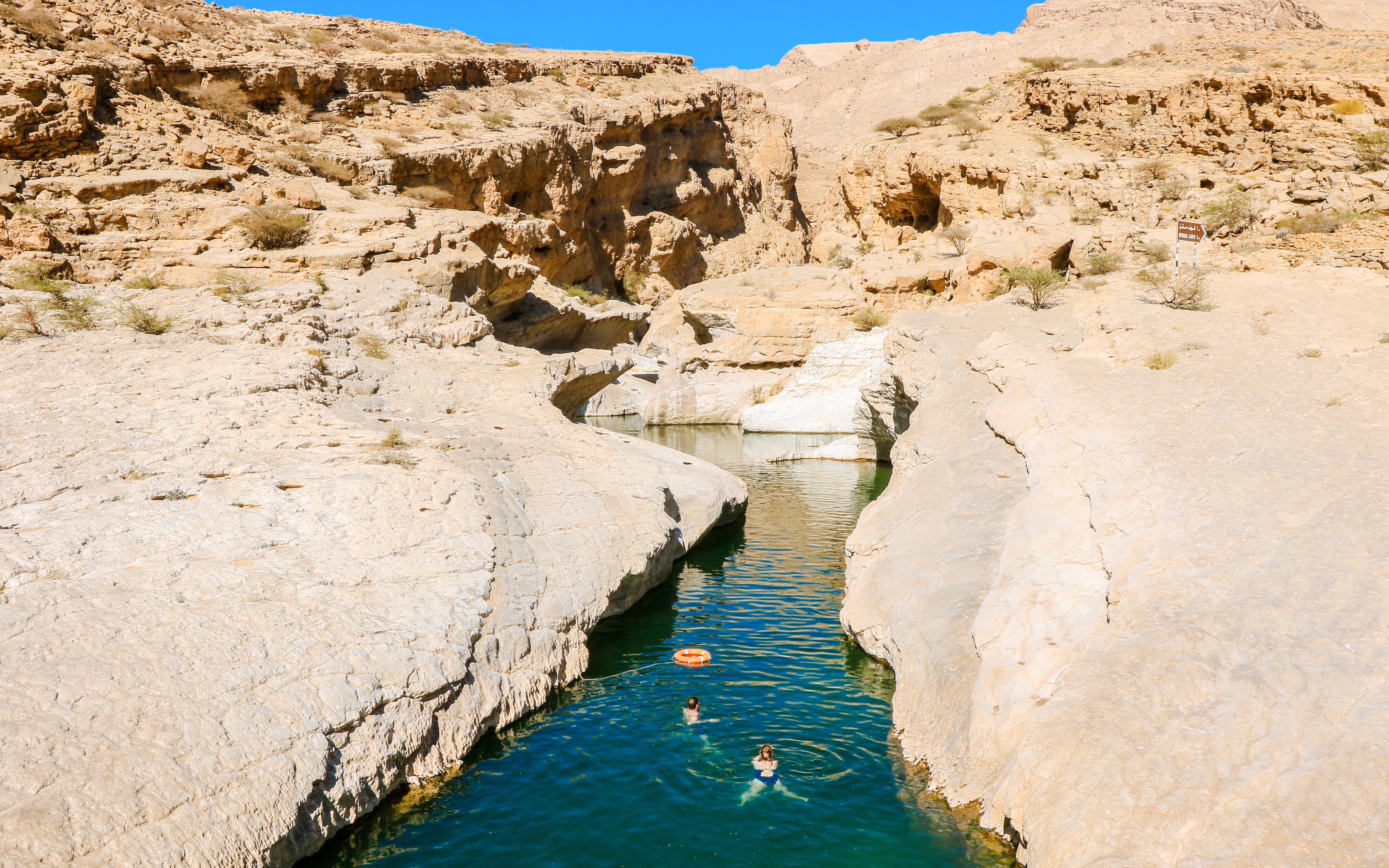 Swimmers in the turquoise waters of Wadi Shab Oasis, surrounded by rocky cliffs in Oman.