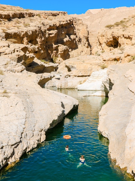 Swimmers in the turquoise waters of Wadi Shab Oasis, surrounded by rocky cliffs in Oman.