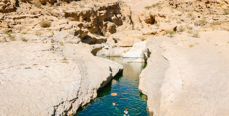 Swimmers in the turquoise waters of Wadi Shab Oasis, surrounded by rocky cliffs in Oman.