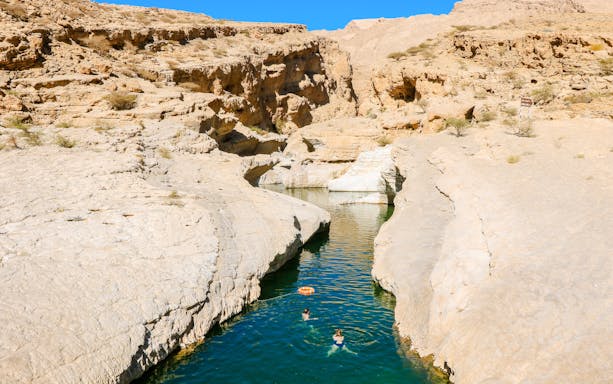 Swimmers in the turquoise waters of Wadi Shab Oasis, surrounded by rocky cliffs in Oman.