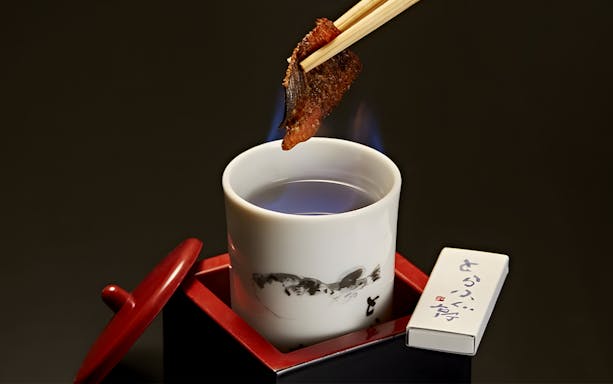 Chopsticks holding grilled fish over a cup at Torafugu-tei Ginza Store.