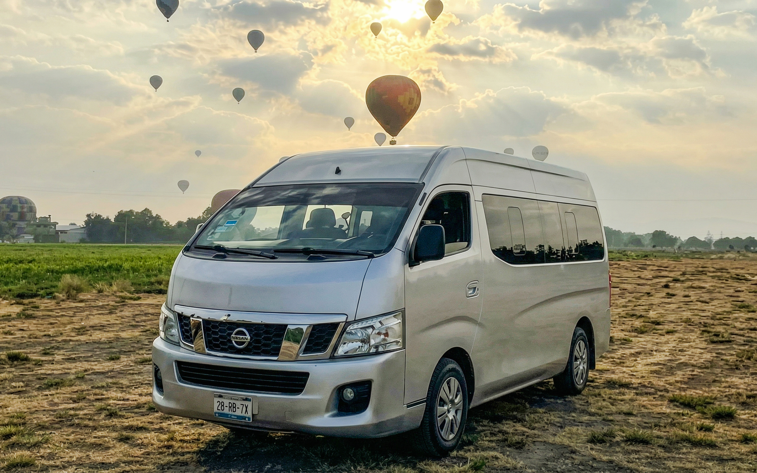 Van parked in a field with hot air balloons in the sky near Mexico City.