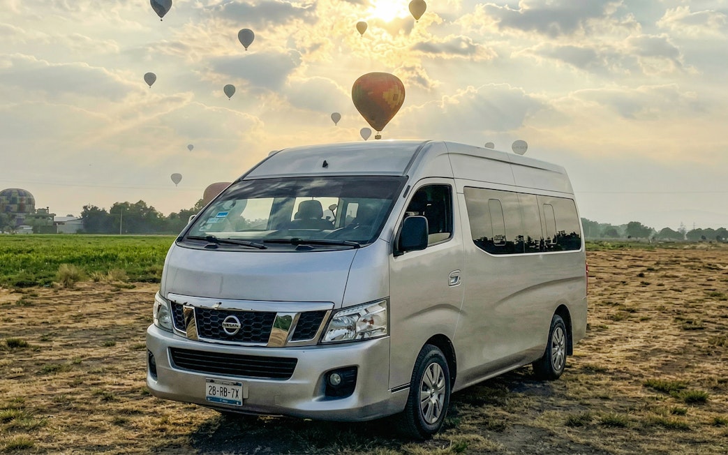 Van parked in a field with hot air balloons in the sky near Mexico City.