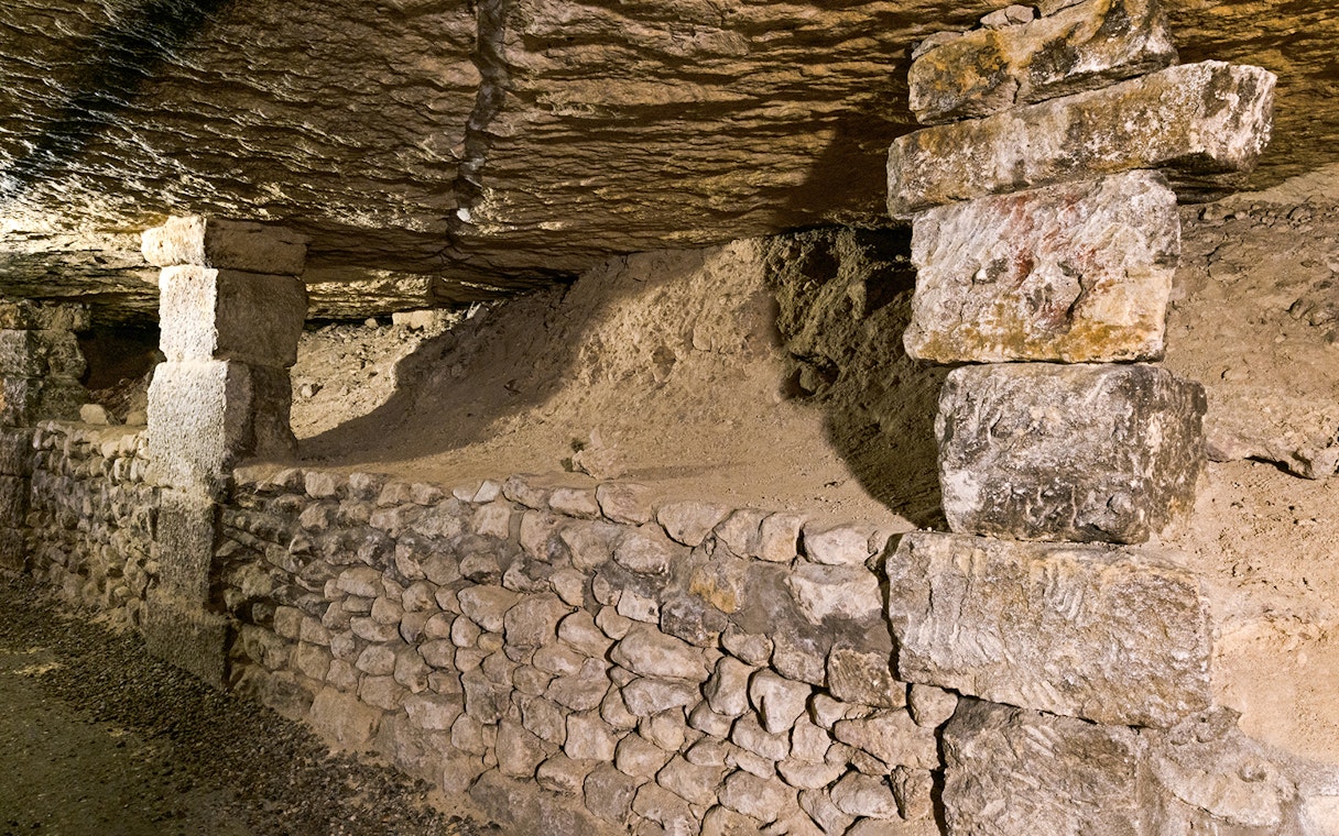 Underground stone passage in the Paris Catacombs with ancient support structures.
