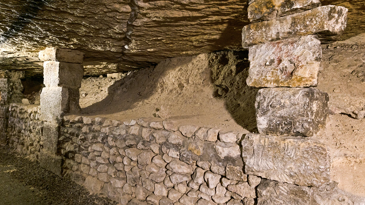 Underground stone passage in the Paris Catacombs with ancient support structures.