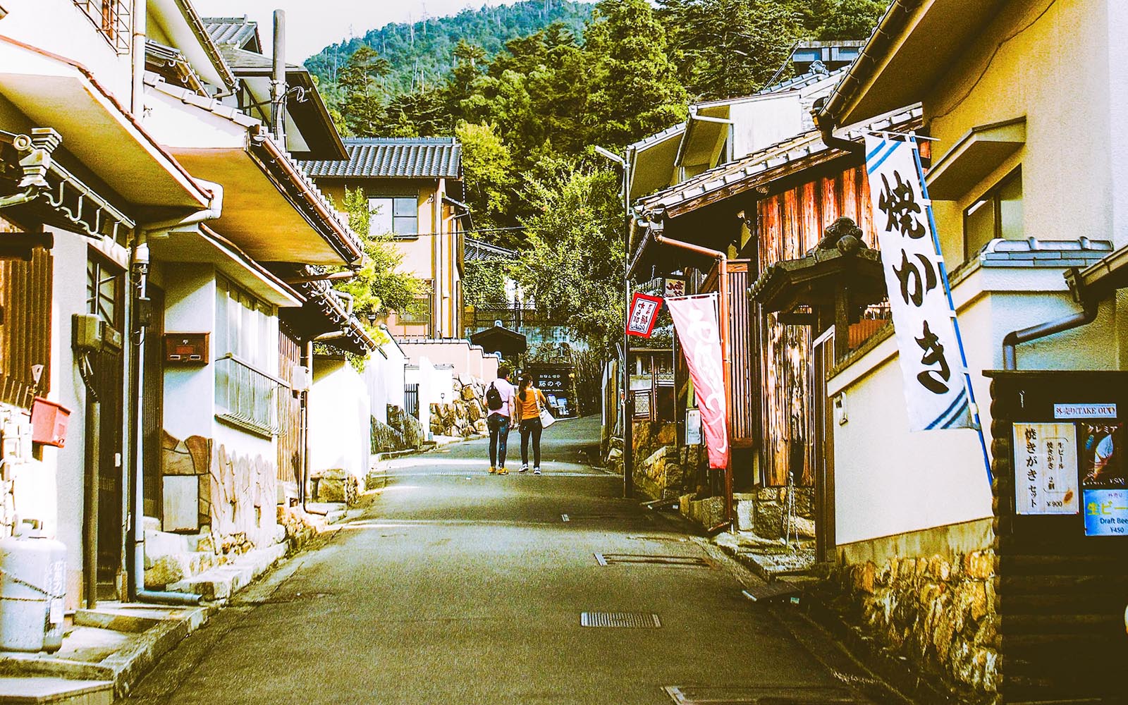 Street view of traditional buildings on Miyajima Island, Japan, with two people walking.