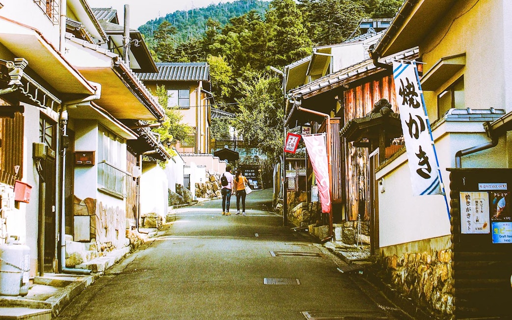 Street view of traditional buildings on Miyajima Island, Japan, with two people walking.