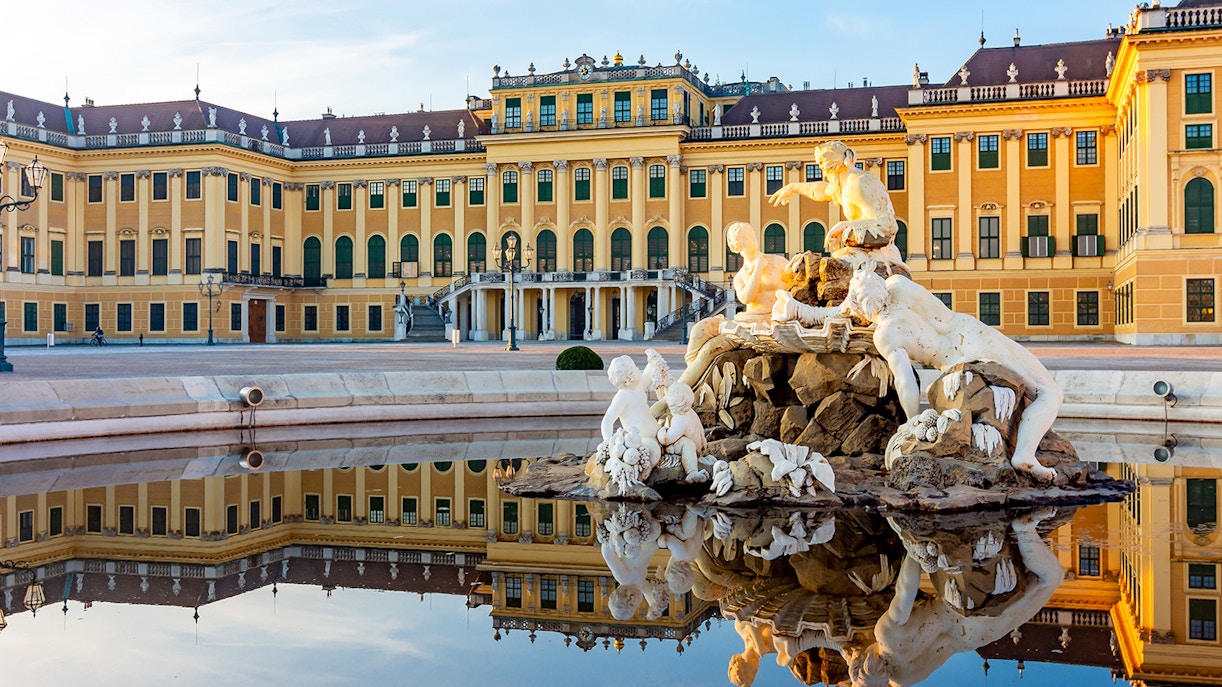 Schönbrunn Palace facade with fountain statues reflecting in Vienna, Austria.