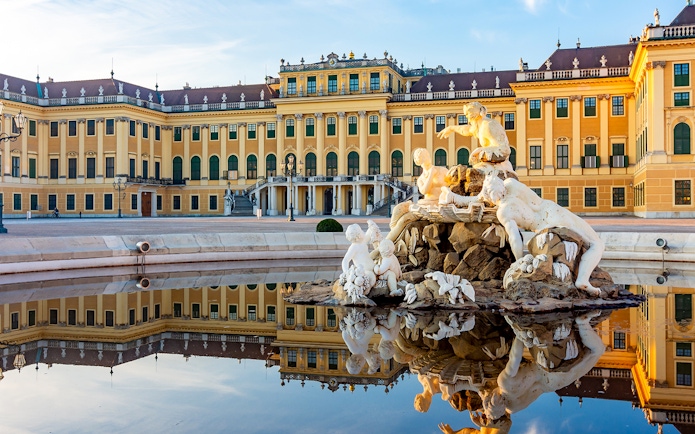 Schönbrunn Palace facade with fountain statues reflecting in Vienna, Austria.