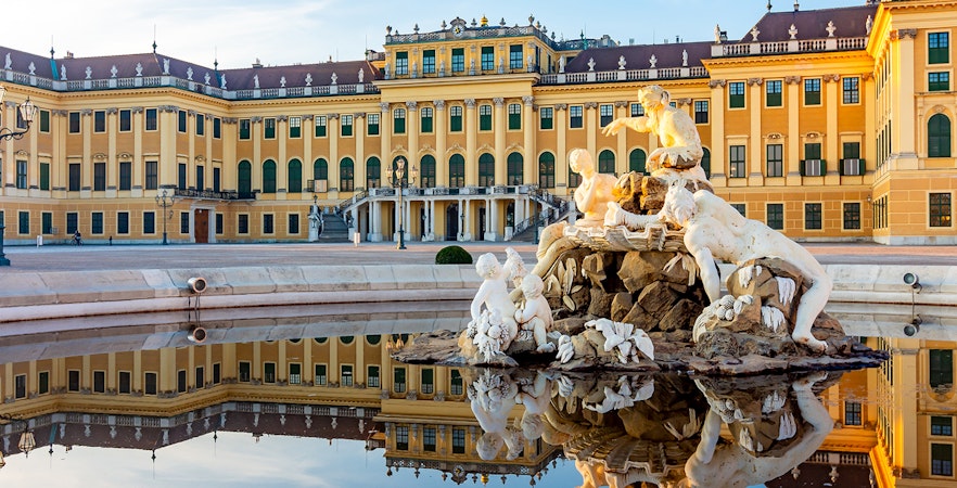 Schönbrunn Palace facade with fountain statues reflecting in Vienna, Austria.