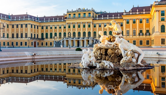 Schönbrunn Palace facade with fountain statues reflecting in Vienna, Austria.