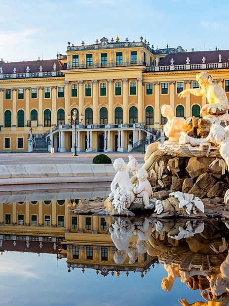 Schönbrunn Palace facade with fountain statues reflecting in Vienna, Austria.