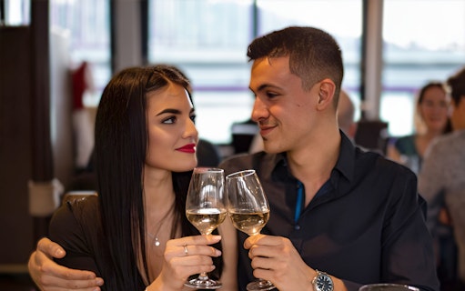 Couple toasting with wine glasses on Budapest cruise with live music.