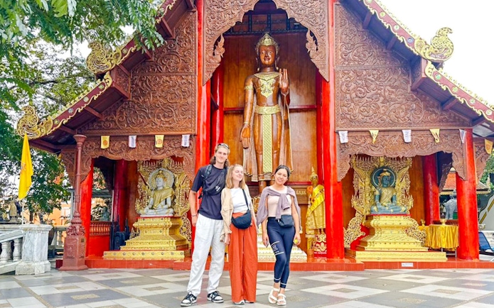 Three people standing in front of a temple with intricate carvings in Chiang Mai, Thailand.