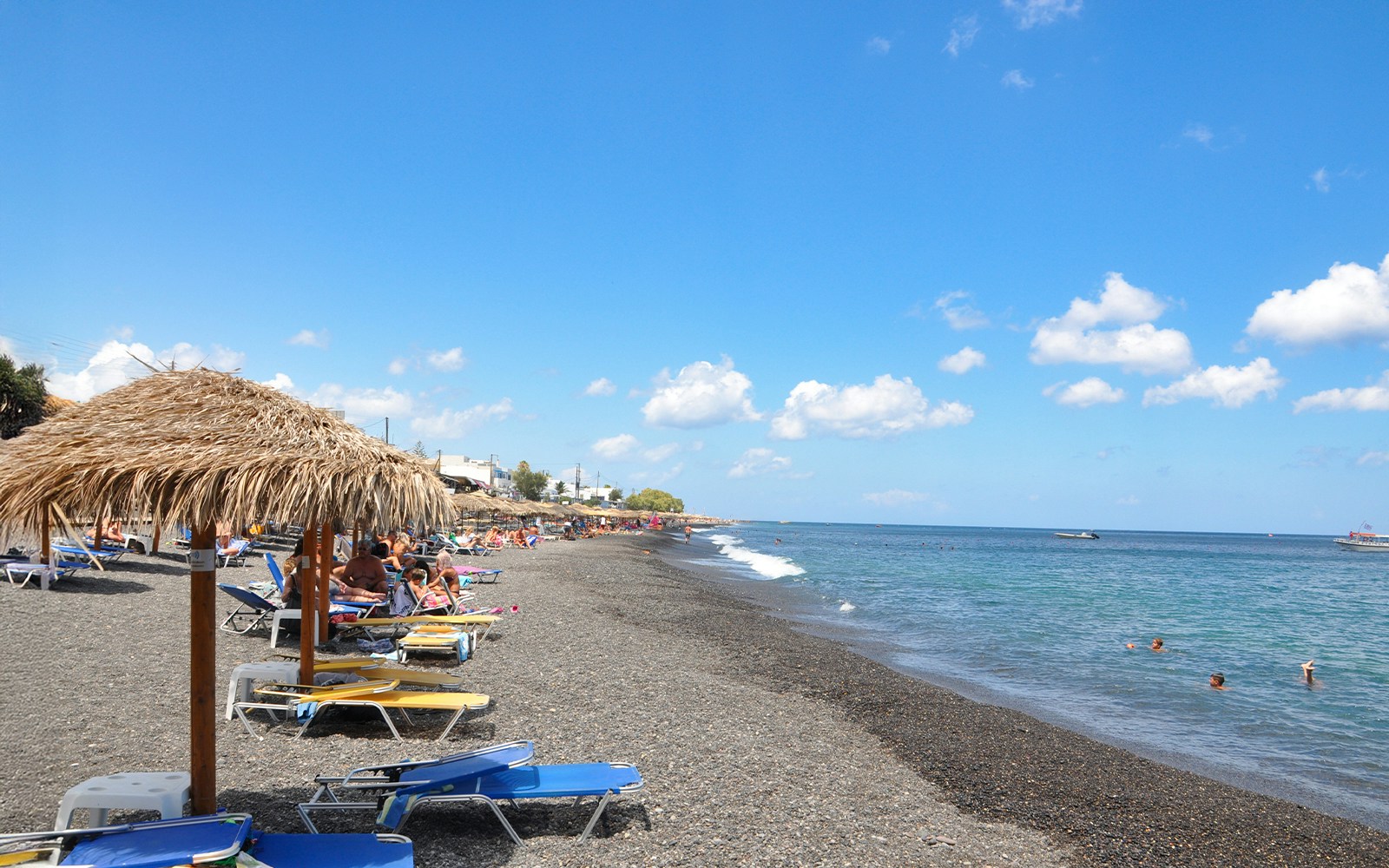 Perivolos Beach in Santorini with black sand and umbrella stands along the shoreline.