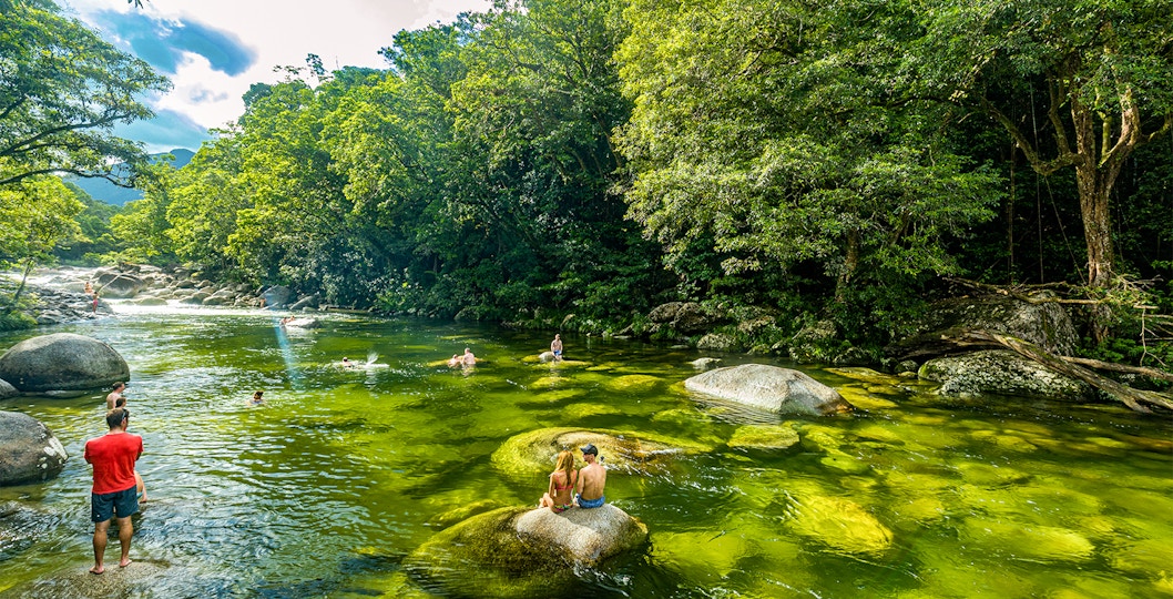 People swimming in a clear river surrounded by lush rainforest in Daintree National Park.