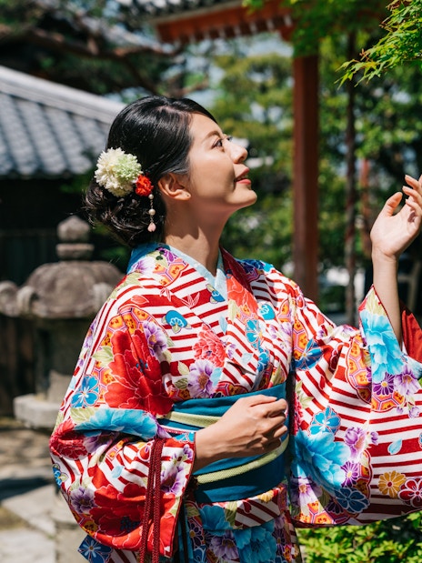 Japanese woman in kimono admiring tree in traditional garden.