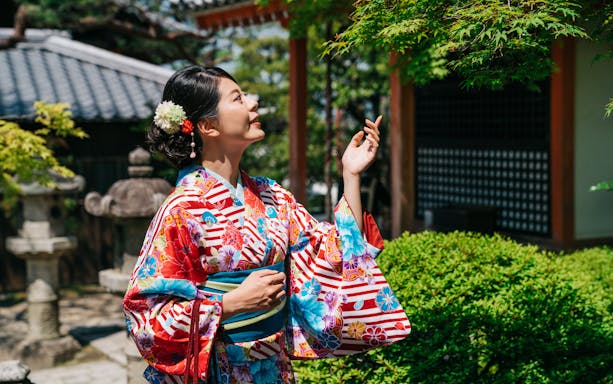 Japanese woman in kimono admiring tree in traditional garden.