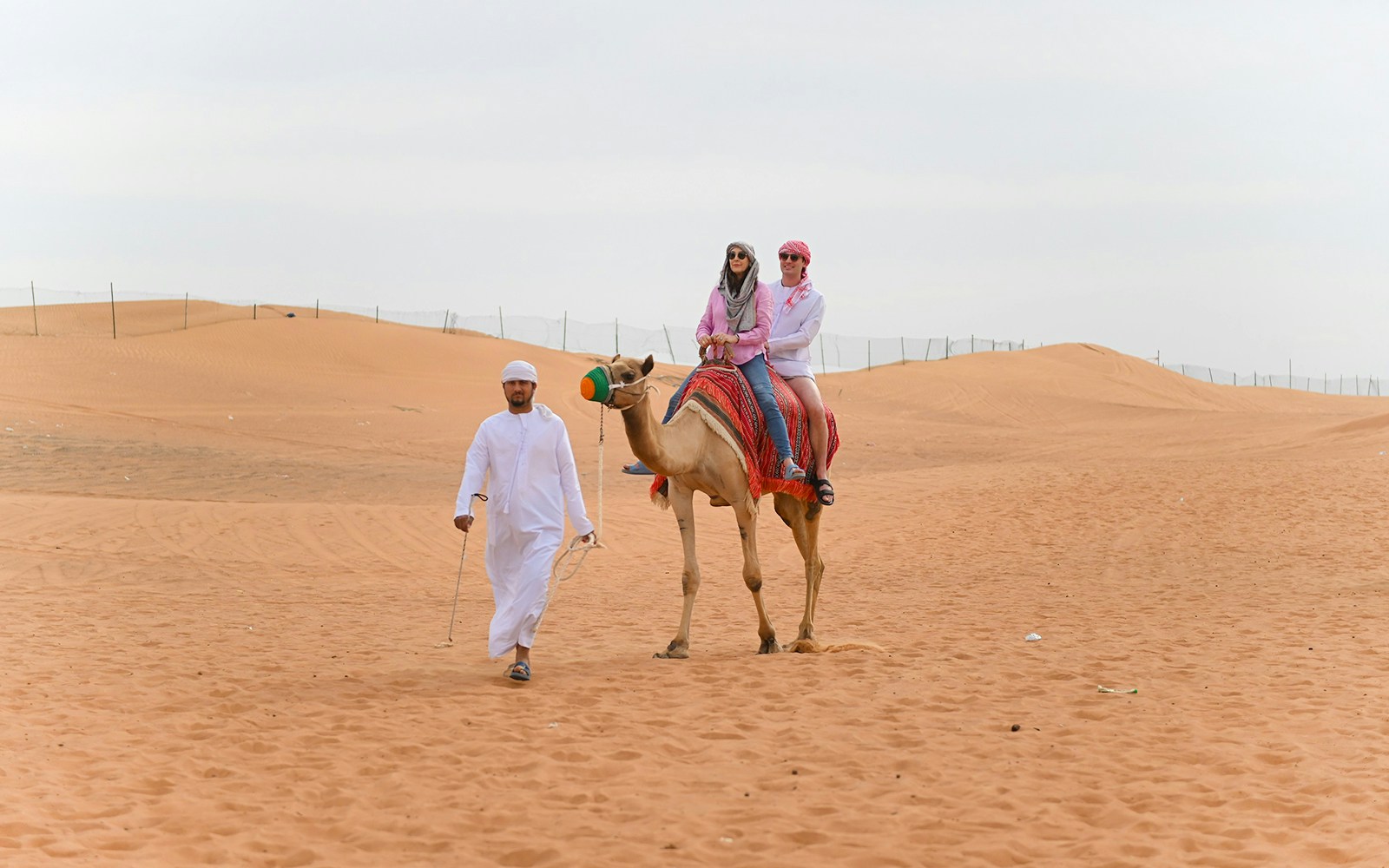 Tourists riding a camel in the Dubai desert led by a guide.