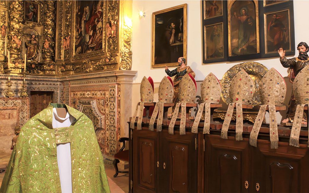 Ornate church interior with collection of bishop mitres and religious paintings.