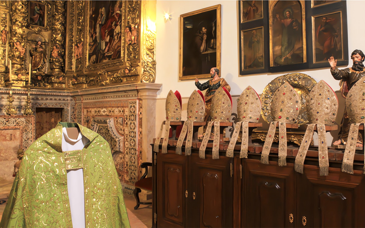 Ornate church interior with collection of bishop mitres and religious paintings.