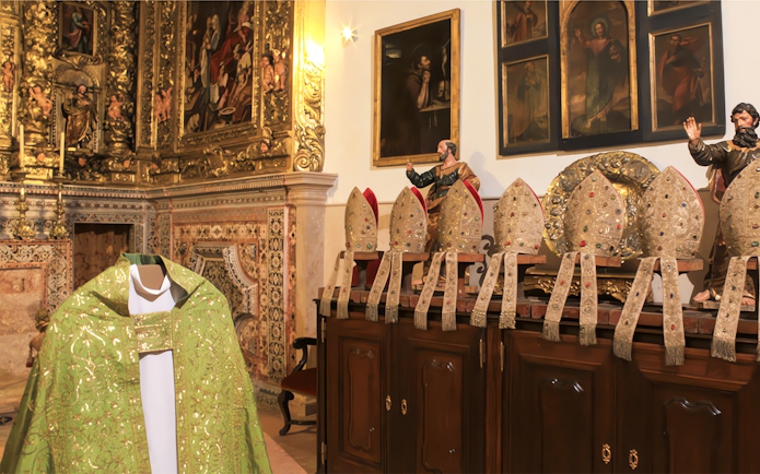 Ornate church interior with collection of bishop mitres and religious paintings.