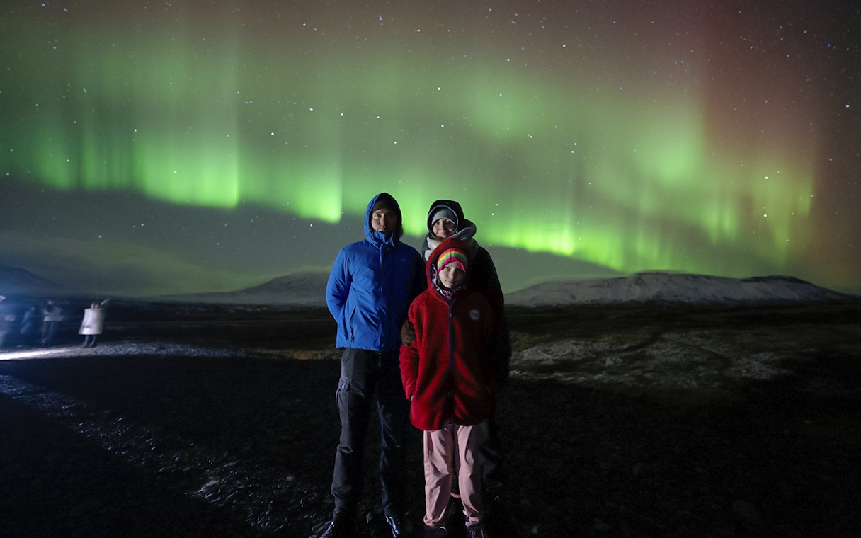 Tourists standing under Northern Lights in Reykjavik, Iceland.
