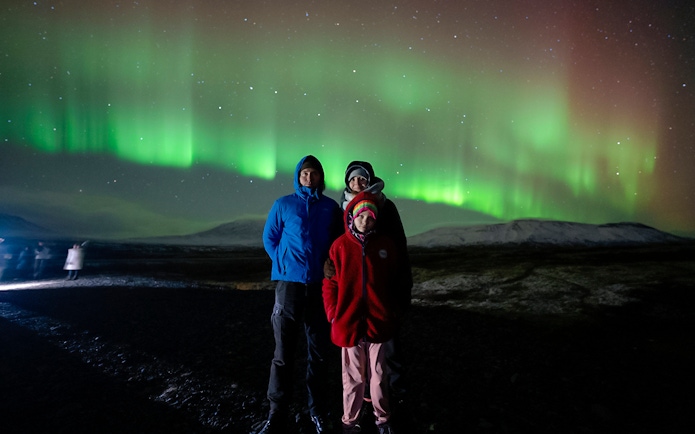 Tourists standing under Northern Lights in Reykjavik, Iceland.