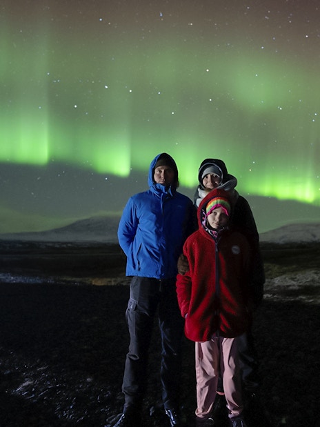 Tourists standing under Northern Lights in Reykjavik, Iceland.