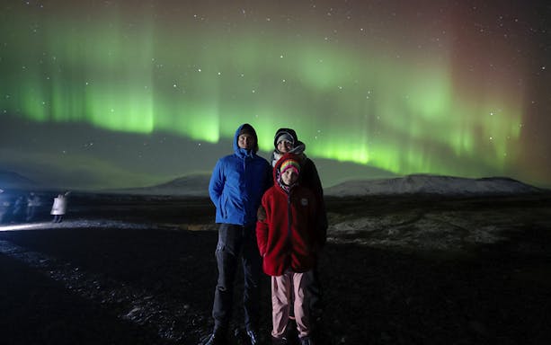 Tourists standing under Northern Lights in Reykjavik, Iceland.