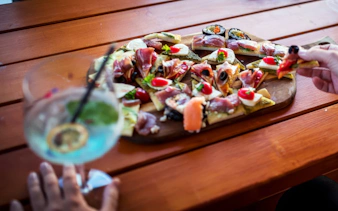 Platter of bite-sized canapés with cured meats, cheese, and cherry tomatoes on a wooden table.
