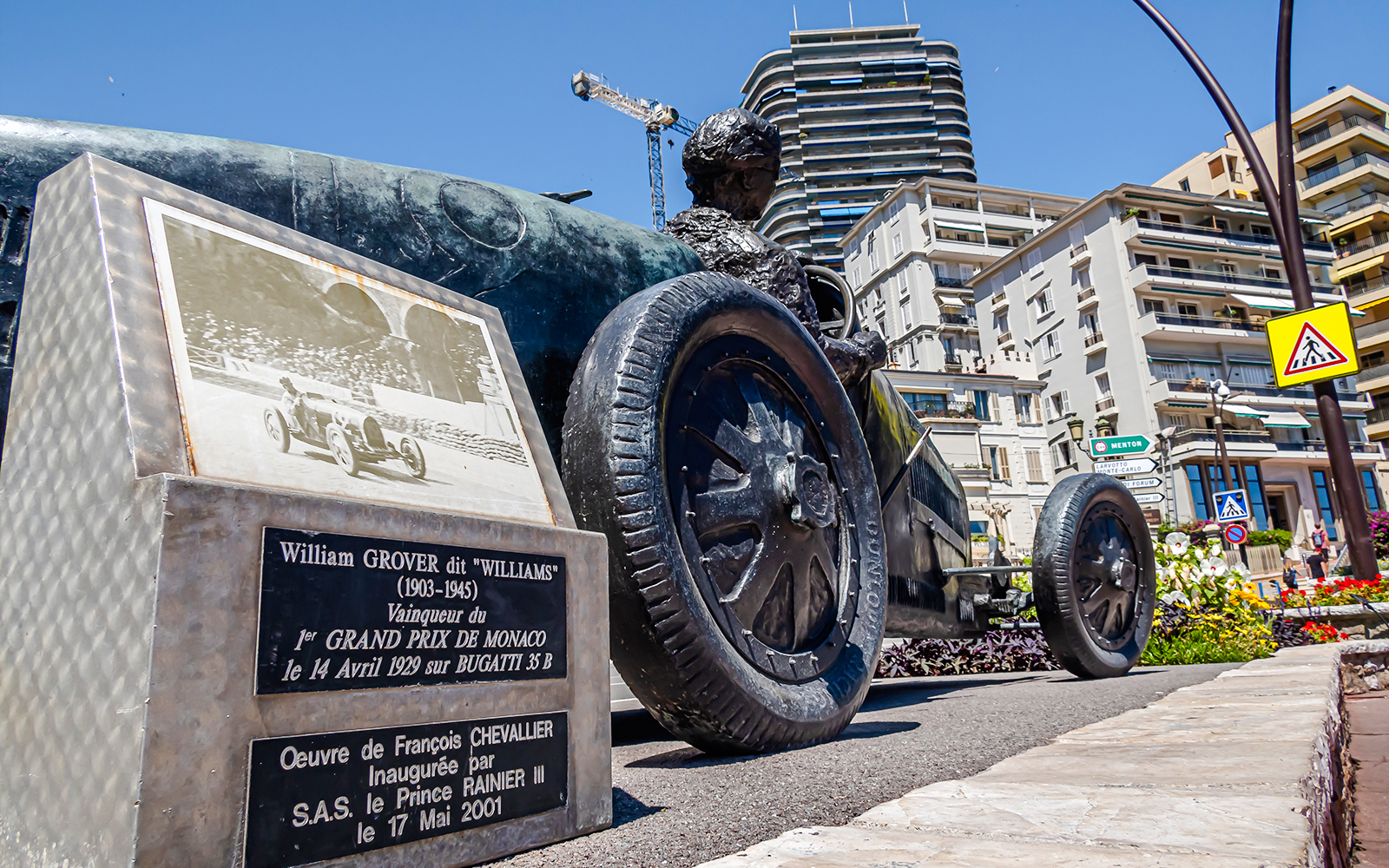 Monaco Formula 1 statue of William Grover in a Bugatti, surrounded by city buildings.