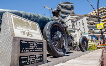 Monaco Formula 1 statue of William Grover in a Bugatti, surrounded by city buildings.