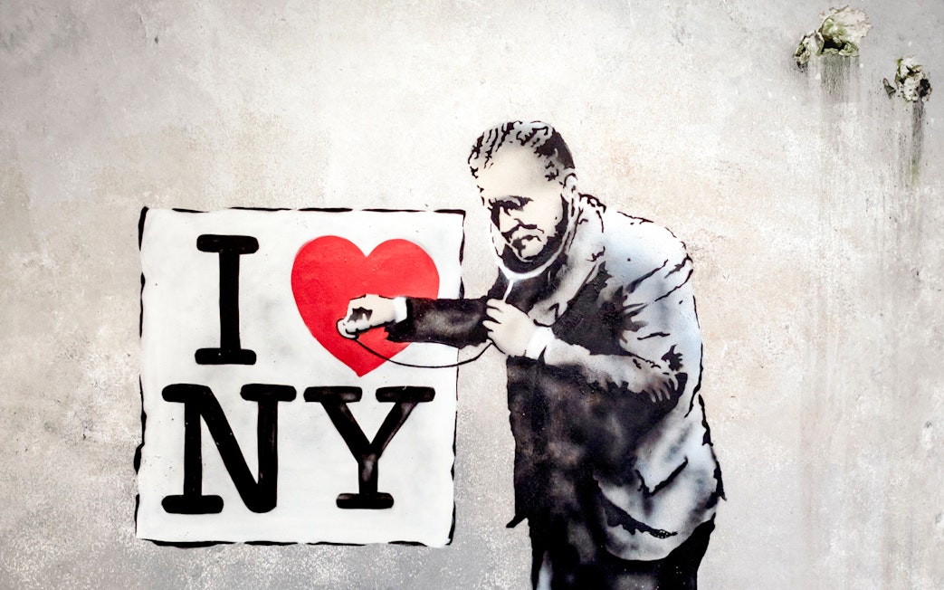 Street art of a man examining "I Love NY" sign with a stethoscope at Banksy Museum.