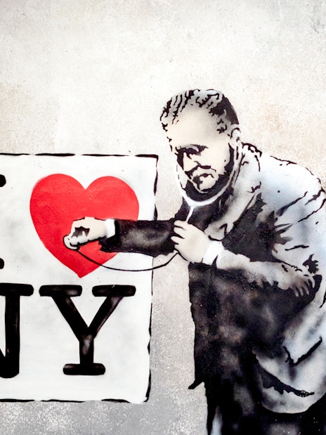 Street art of a man examining "I Love NY" sign with a stethoscope at Banksy Museum.