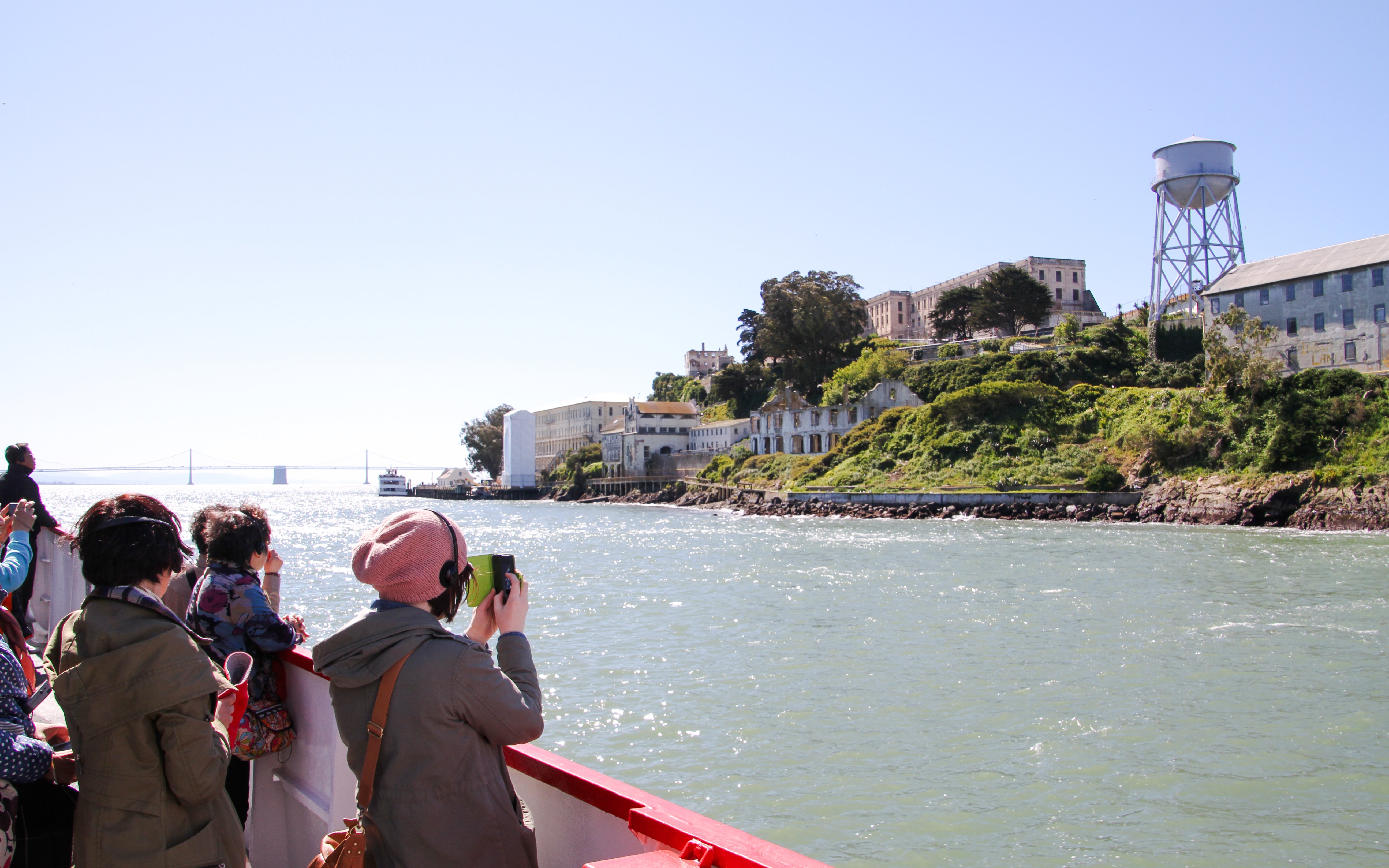 Tourists on a boat viewing Alcatraz Island with Golden Gate Bridge in the background.
