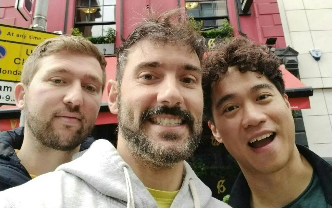 Three people smiling in front of a red building in Belfast during a city exploration game.