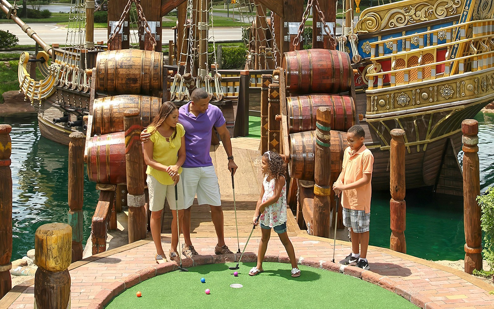 Family playing mini-golf near pirate ship at Pirate's Cove Adventure Golf.