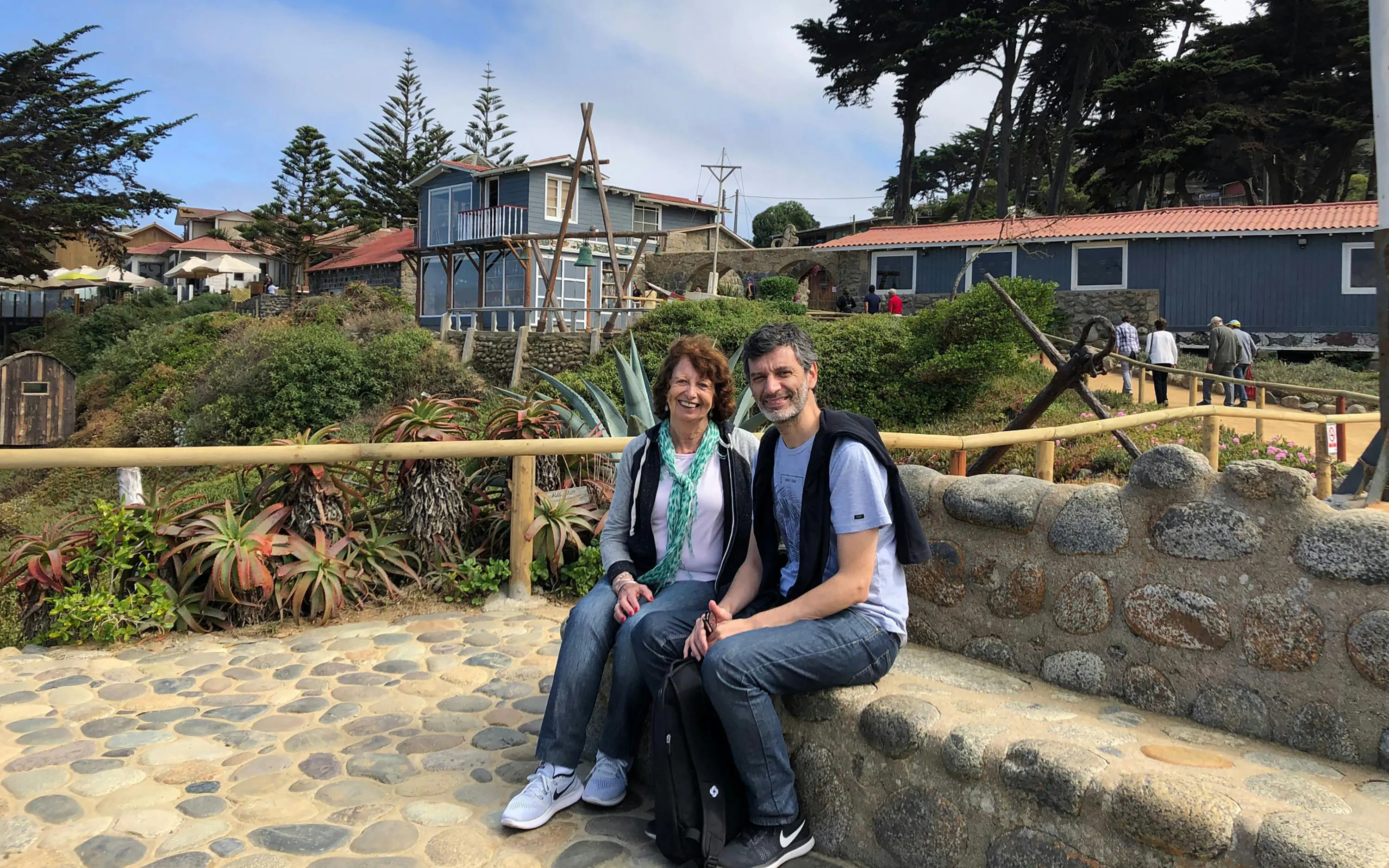 Tourists sitting outside Pablo Neruda's house in Chile with gardens and coastal views.