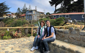 Tourists sitting outside Pablo Neruda's house in Chile with gardens and coastal views.
